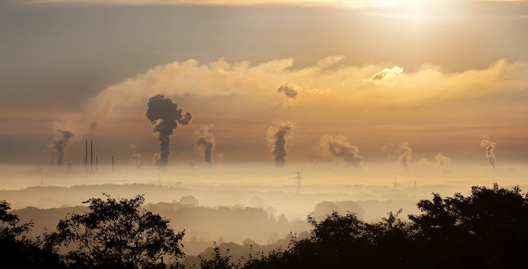 Smoke rising from factory chimneys at sunrise, symbolizing pollution and environmental impact.